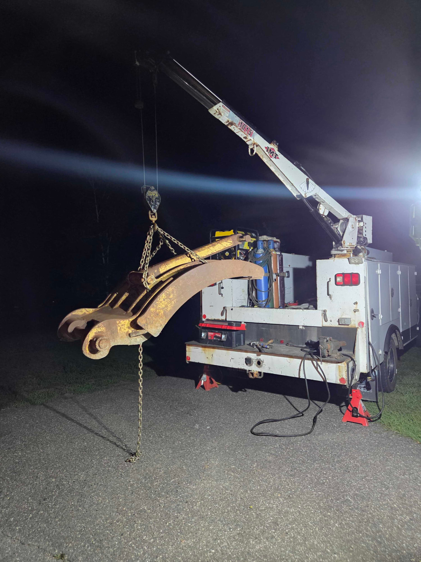 Service truck crane lifting an excavator boom during a nighttime emergency repair