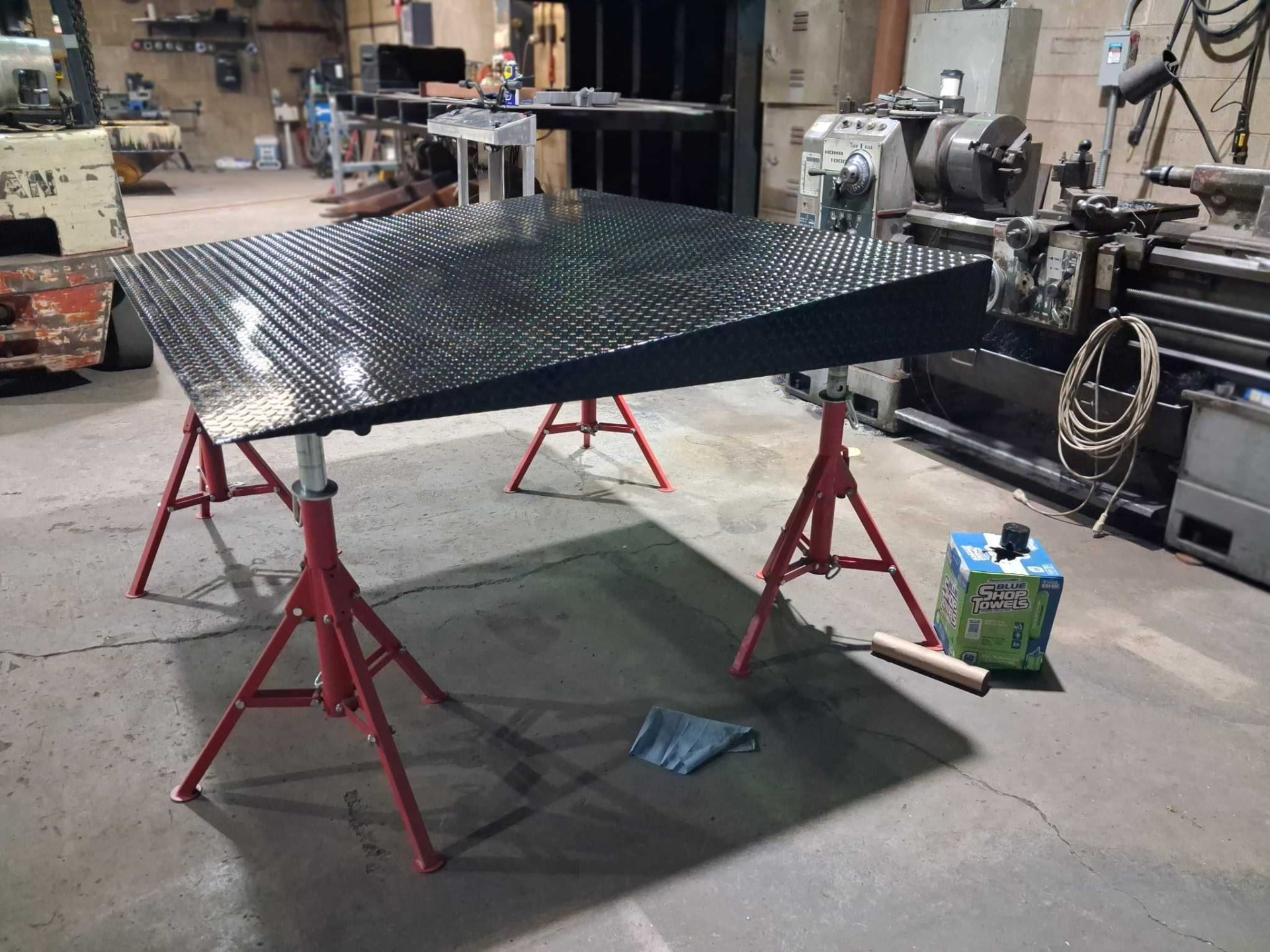 Fabricated diamond plate steel ramp resting on red adjustable pipe stands beside a metal lathe