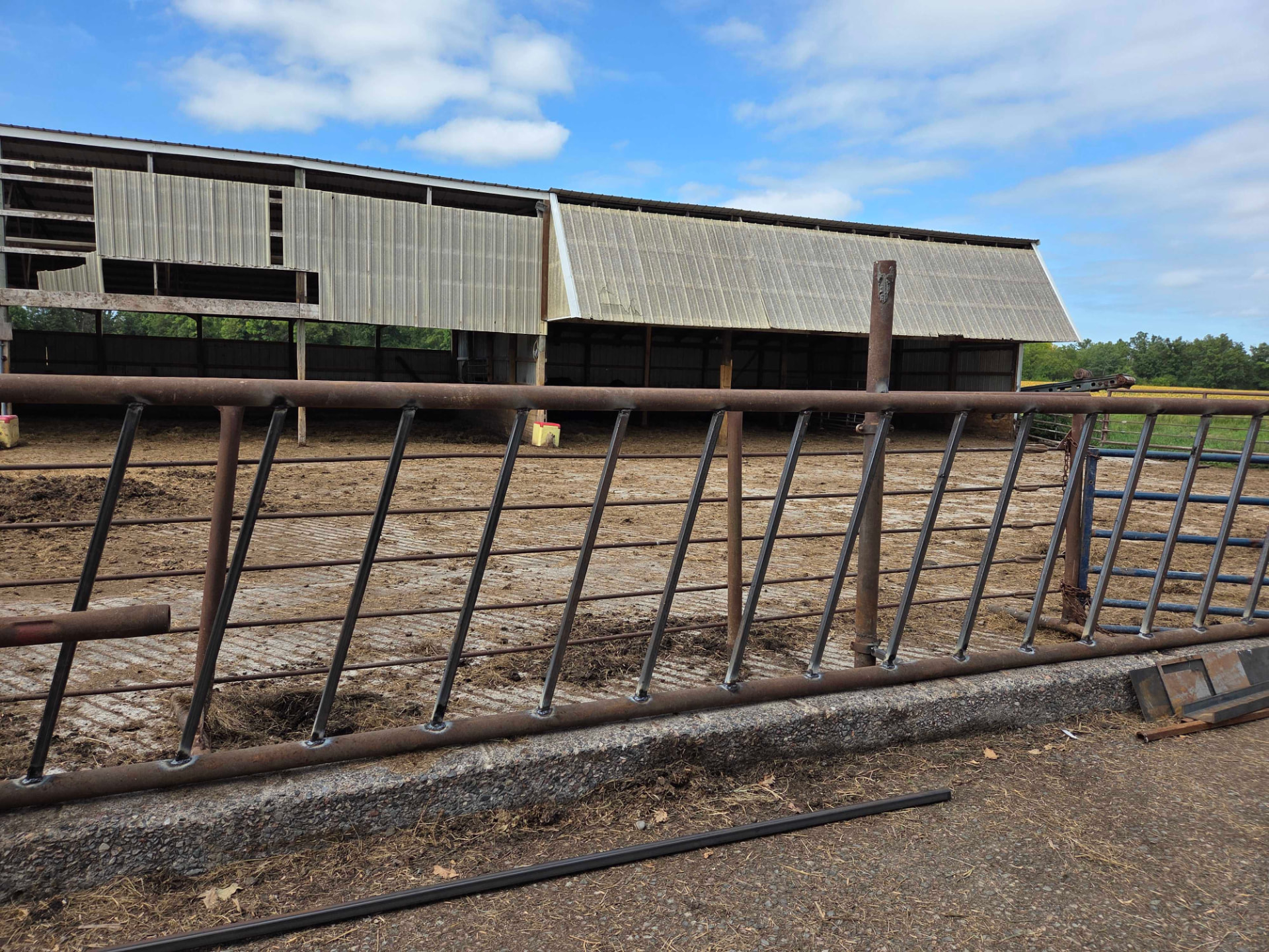 Repaired steel farm fence gate with welded vertical rails in front of a barn