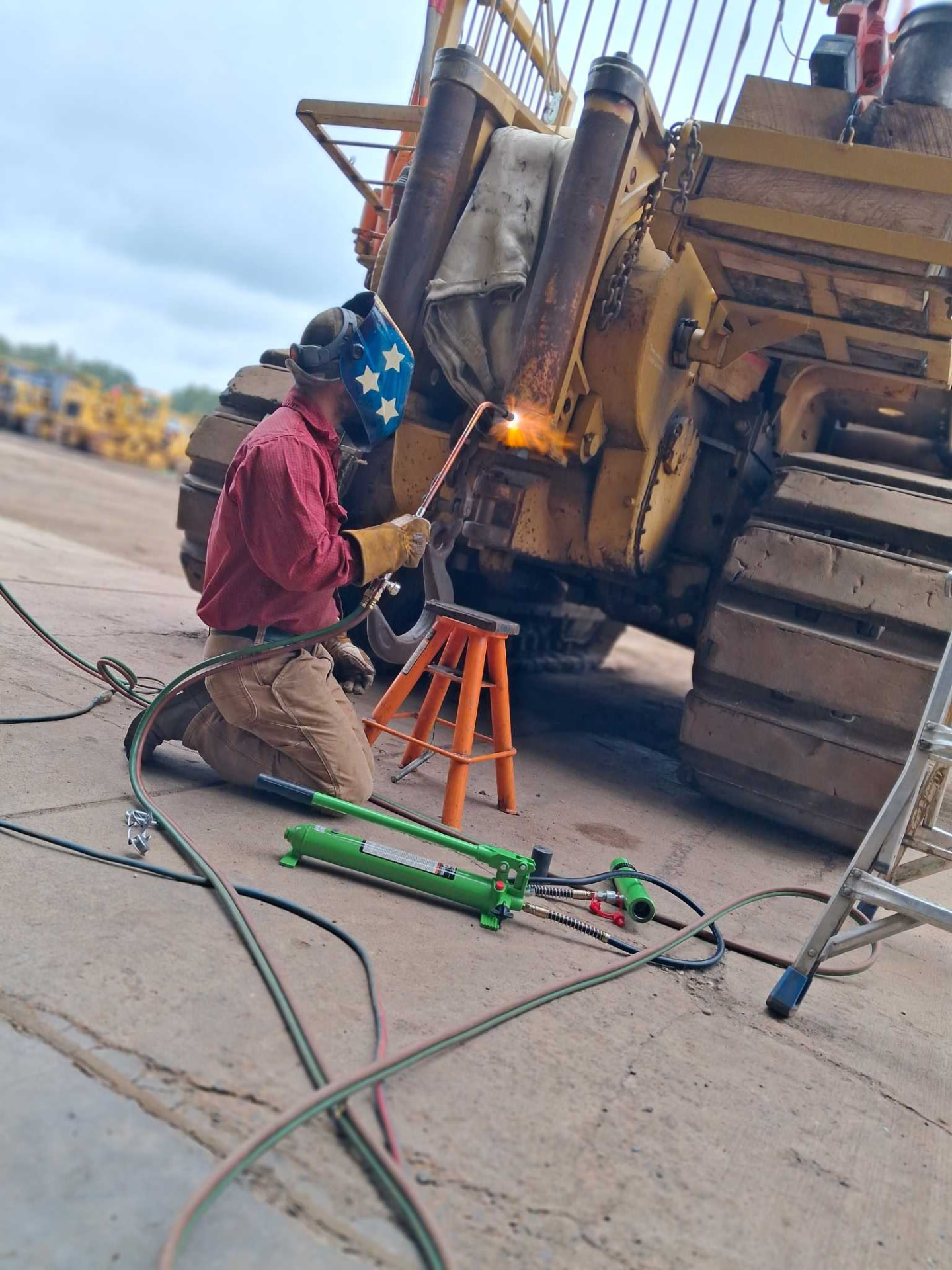 Welder using a torch on a CAT excavator boom and stick during a field repair