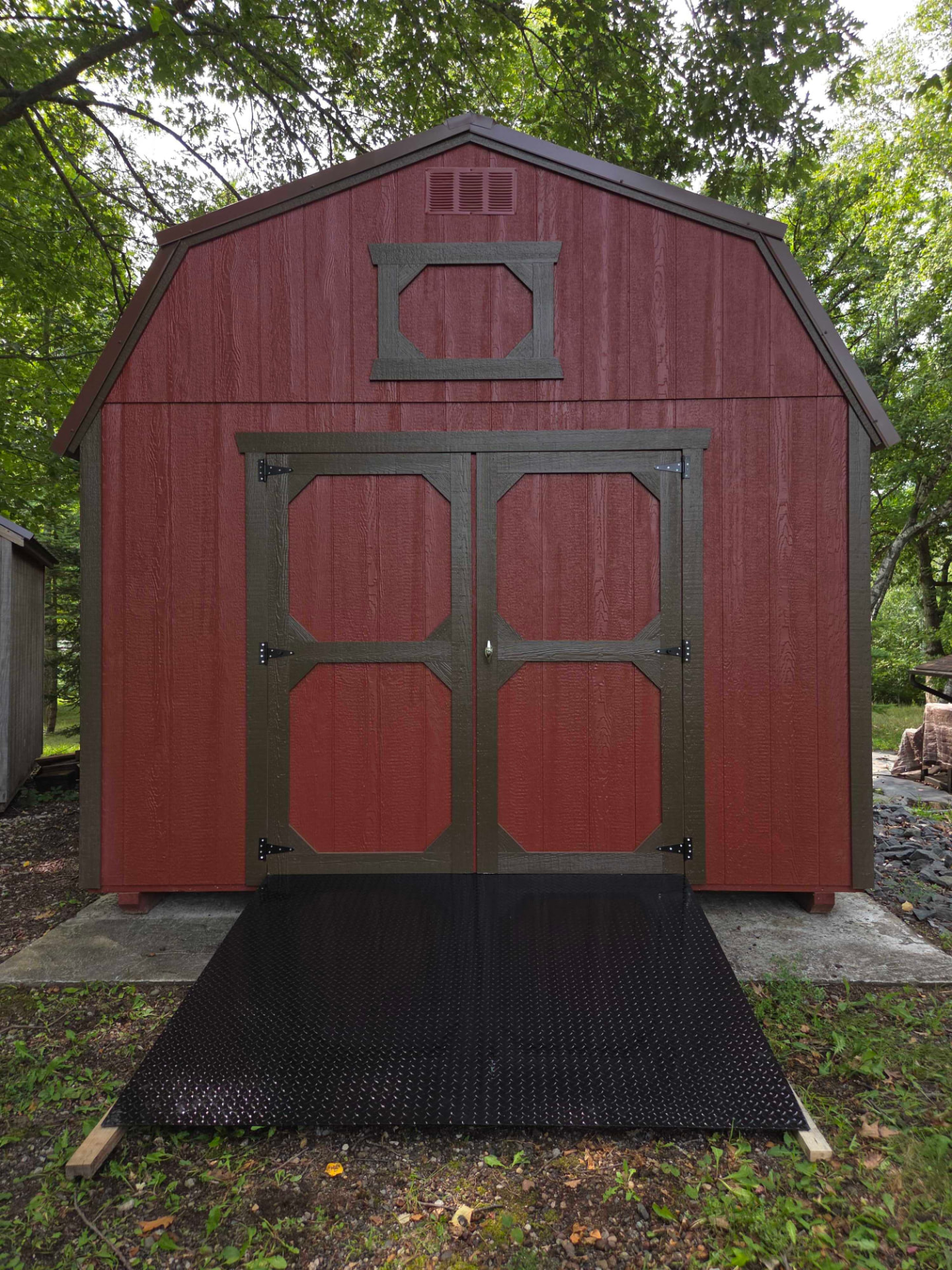 Red barn-style shed with a black diamond plate steel ramp leading to the double doors