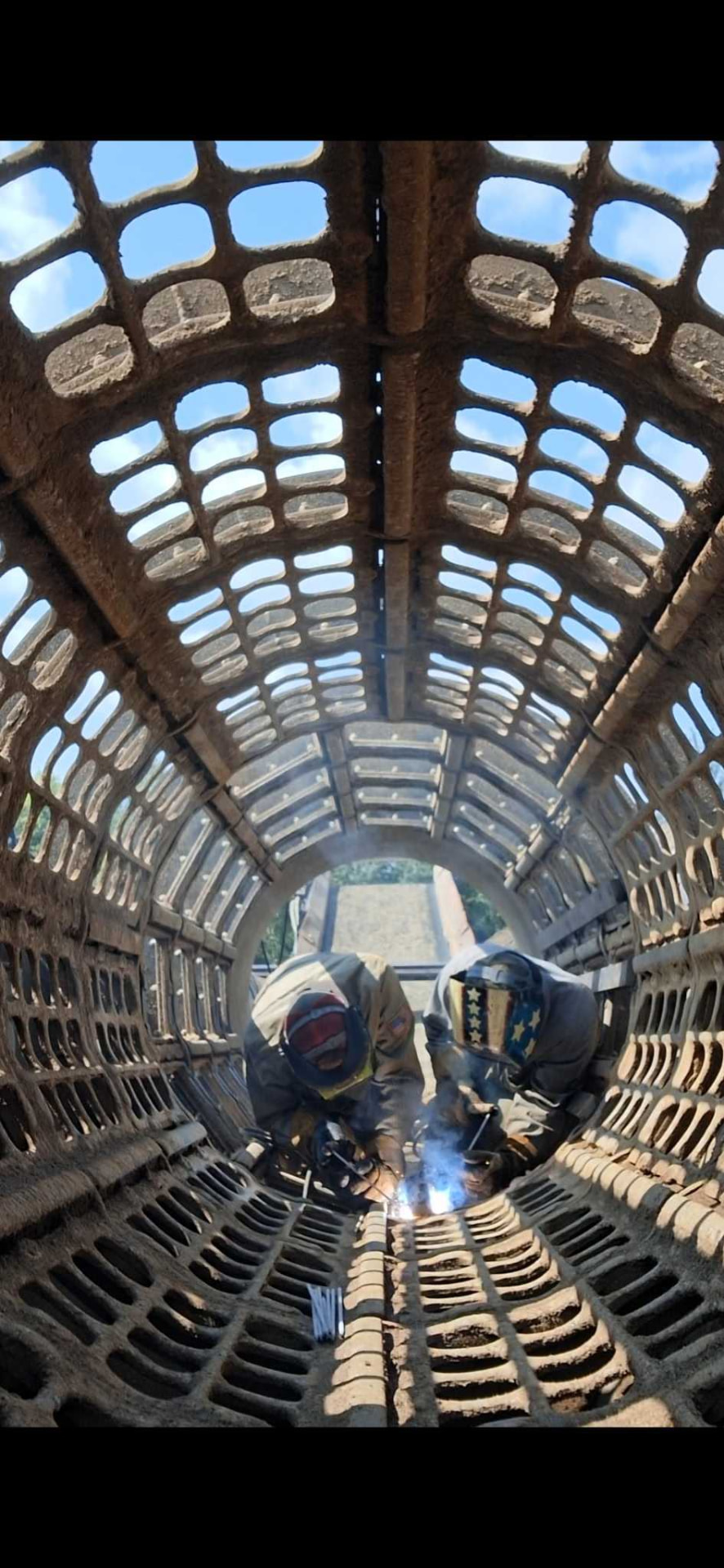 Two welders welding inside a large cylindrical trommel screen at a quarry