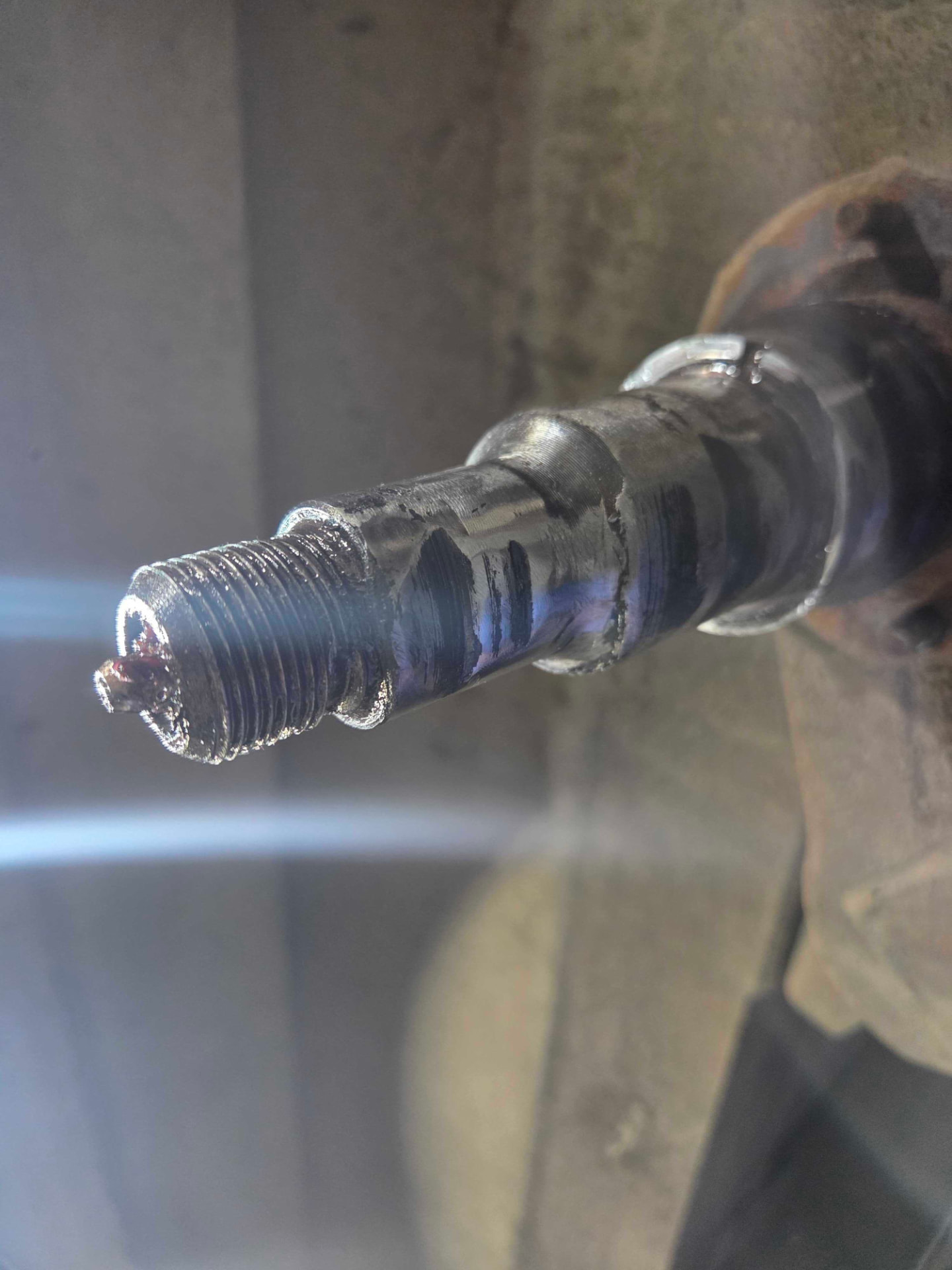Close-up of a rebuilt and machined axle spindle with visible weld build-up and threaded end